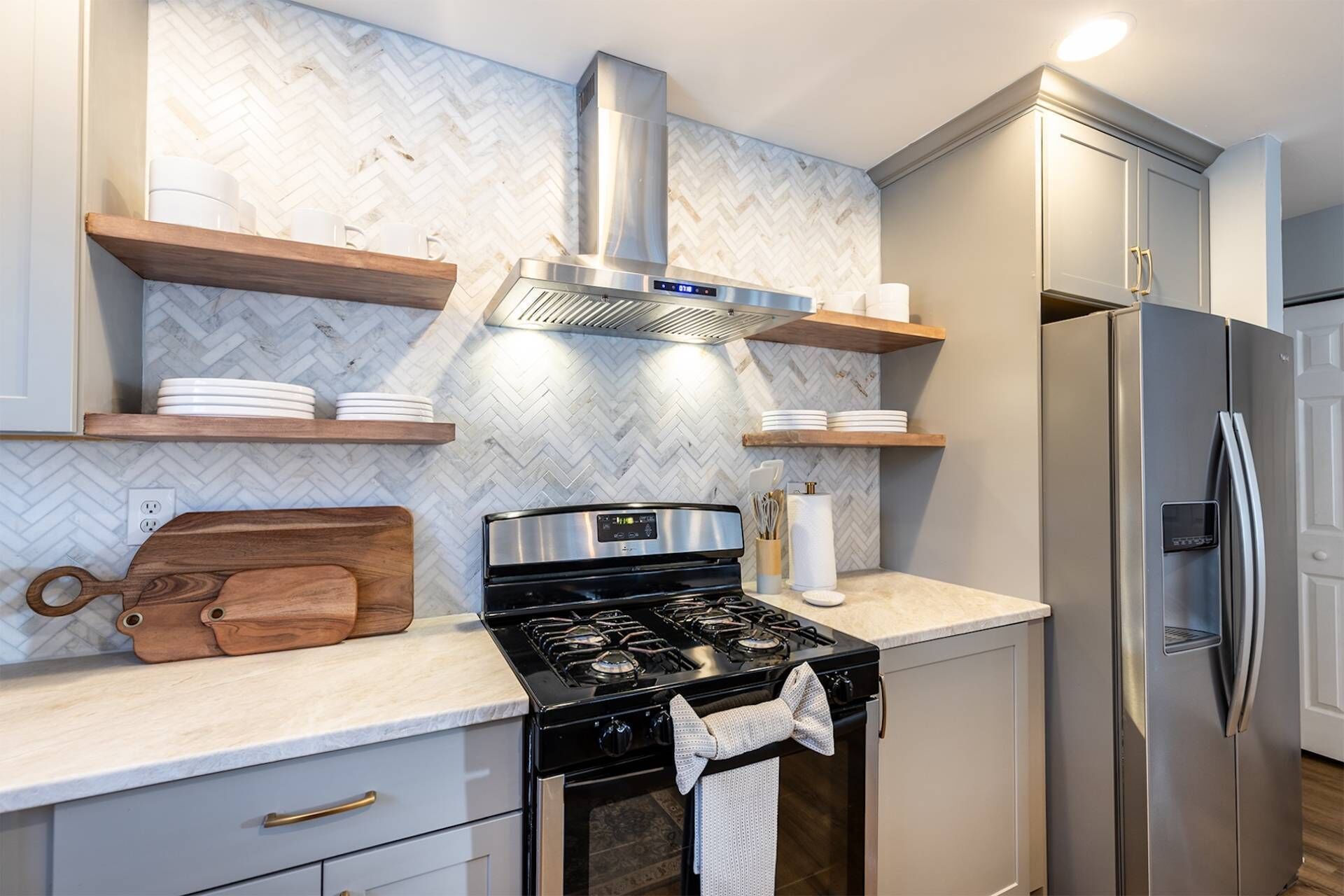 Una cocina moderna con estufa a gas, electrodomésticos de acero inoxidable, estantes de madera y salpicadero de baldosas en espiga.