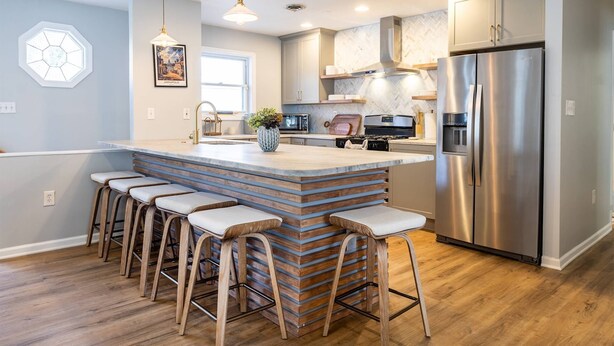 A modern kitchen with a central island, stainless steel appliances, and wooden bar stools.