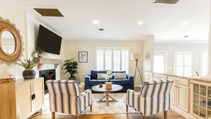 A spacious living area with a blue sofa, two striped armchairs, a round coffee table, and a wooden cabinet.