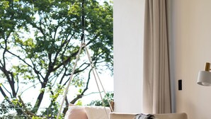 A modern living room with a hanging swing chair, a white sofa, and a view of greenery outside.