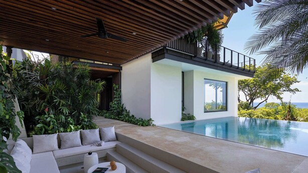 A modern outdoor living area with a pool, a wooden ceiling, and a view of the ocean.
