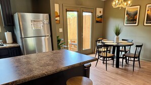 A modern kitchen with a granite countertop, stainless steel refrigerator, wooden stools, and a dining area with a round table and chairs. - Townhome near Dollywood w/ Hot Tub•June Promo (Sevierville)