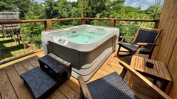 A hot tub on a wooden deck with chairs and a table, surrounded by greenery and a wooden fence. - Townhome near Dollywood w/ Hot Tub•June Promo (Sevierville)