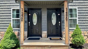 A two-story house with a front porch, two black doors with decorative glass panels, and stone accents on the lower part of the walls. - Townhome near Dollywood w/ Hot Tub•June Promo (Sevierville)