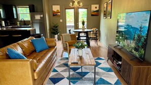 A modern living room with a leather sofa, a coffee table, a TV, and a dining area with chairs and a table. - Townhome near Dollywood w/ Hot Tub•June Promo (Sevierville)