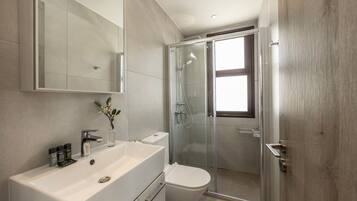 A modern bathroom with a large mirror, a white sink, a toilet, and a glass-enclosed shower.