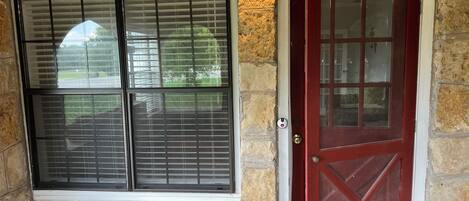 A stone exterior with a red door and two windows with blinds.