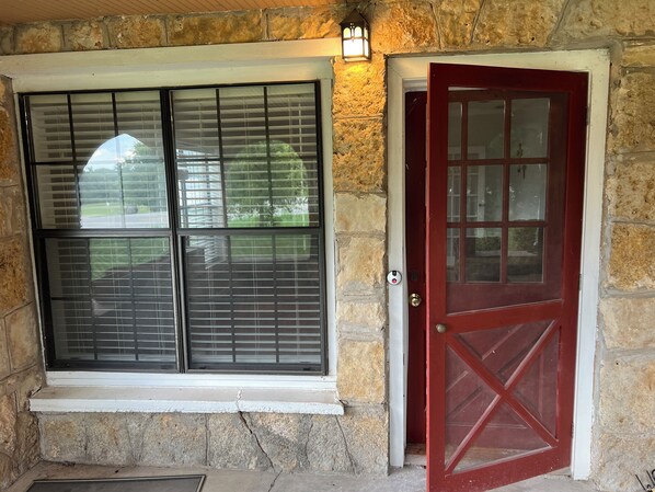 A stone exterior with a red door and two windows with blinds.