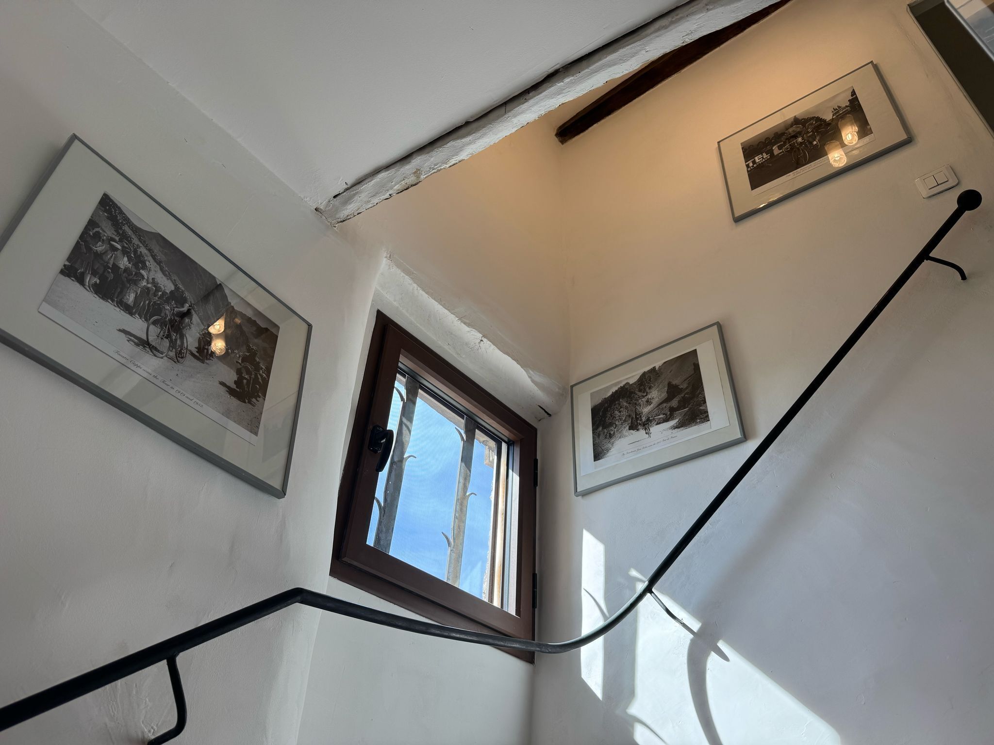 Een trap met een leuning, een raam en drie ingelijste foto's aan de muur.