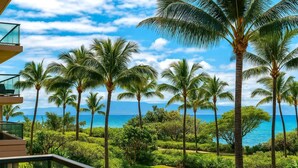 A resort with a view of the ocean, palm trees, and a building with a balcony.