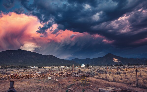 A rural landscape with mountains, a wooden fence, and a house in the distance. - Hidden Haven: Open Concept Inside, Dramatic Views Outside (Questa)