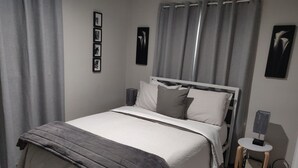 A neatly made bed with a grey blanket, a white headboard, and grey curtains. - Hidden Haven: Open Concept Inside, Dramatic Views Outside (Questa)