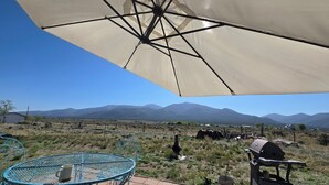 A patio with a table and chairs, a barbecue grill, and a large umbrella providing shade. - Hidden Haven: Open Concept Inside, Dramatic Views Outside (Questa)
