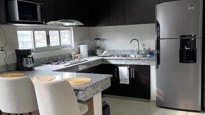 Une cuisine moderne avec des meubles de couleur sombre, un réfrigérateur en acier inoxydable, un four à micro-ondes, une machine à café et un coin bar avec des tabourets.