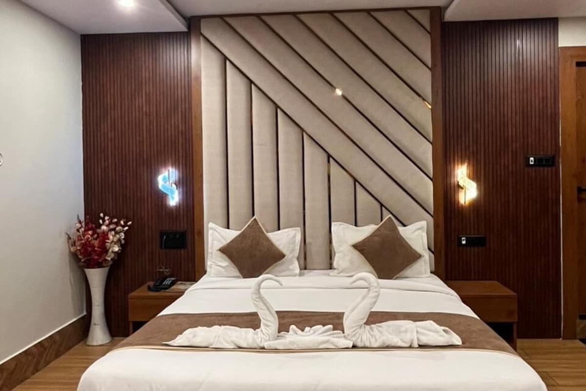A modern hotel room with a large bed, wooden paneling, a ceiling fan, and a nightstand with a vase of flowers.