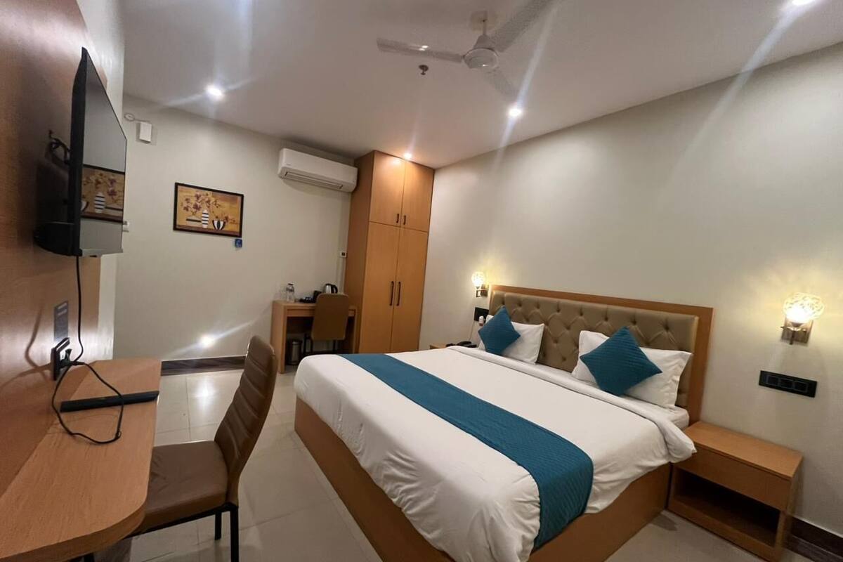 A hotel room with a bed, bedside table, chair, desk, and a television.
