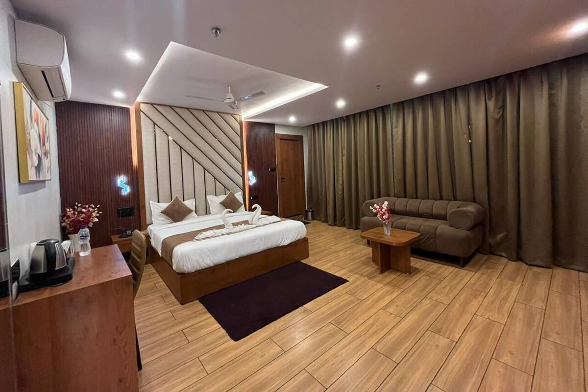 A modern hotel room with a bed, a sofa, a desk, and a coffee machine.