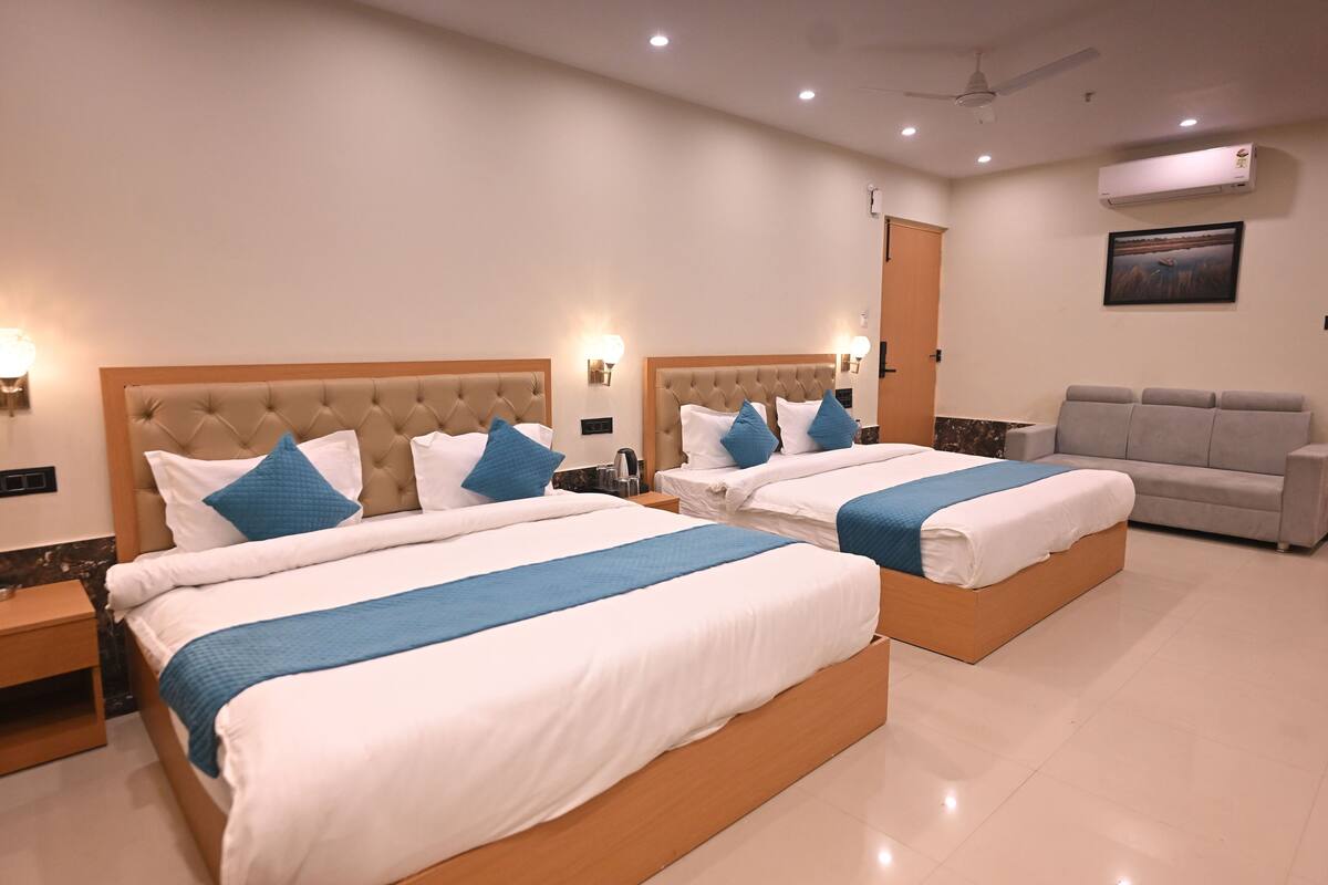 A hotel room with two beds, a sofa, and a ceiling fan.