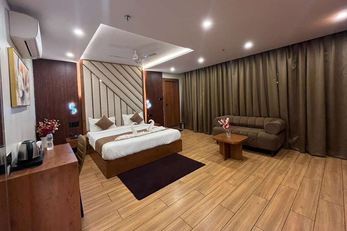 A modern hotel room with a bed, a sofa, a desk, and a coffee machine.