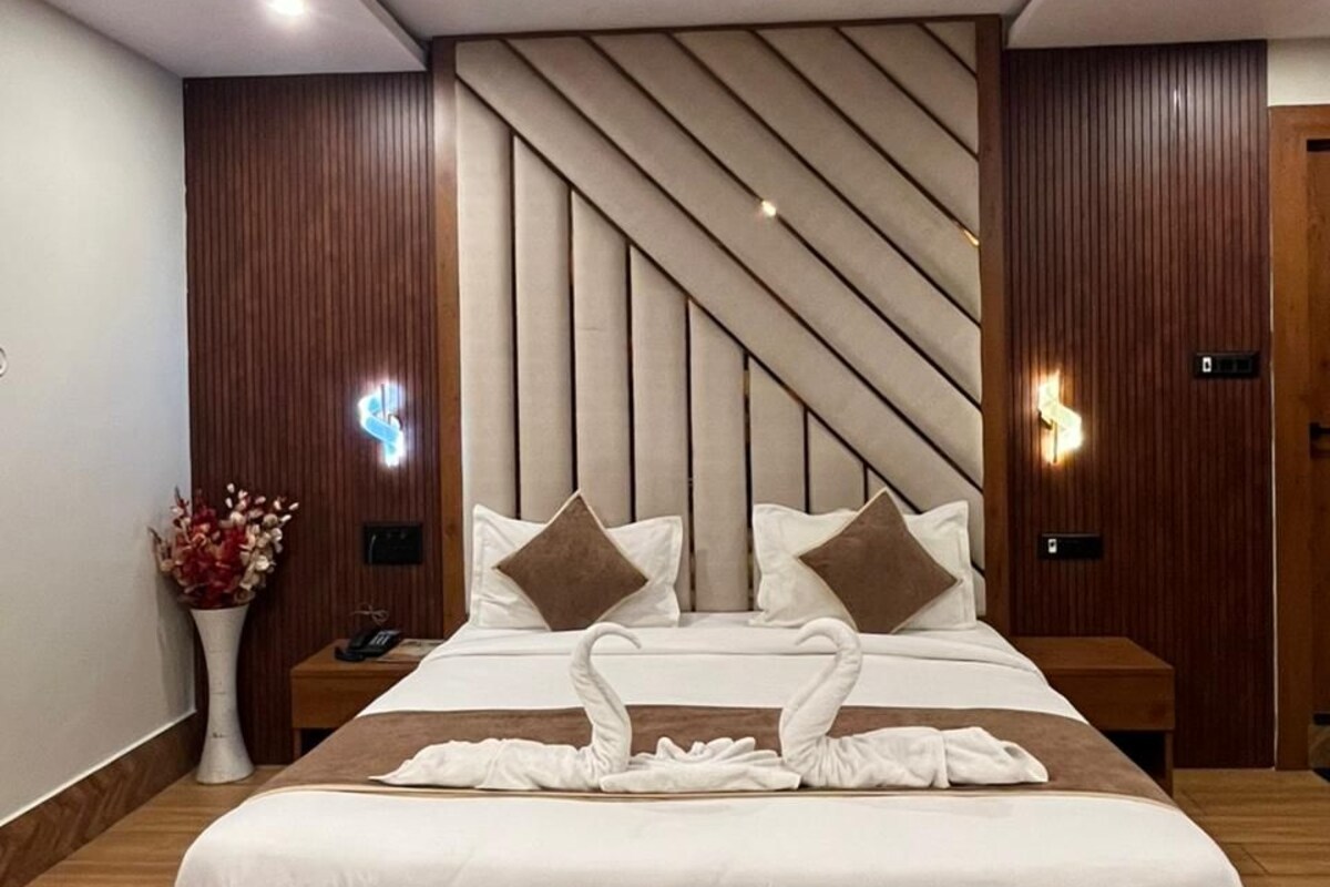 A modern hotel room with a large bed, wooden paneling, a ceiling fan, and a nightstand with a vase of flowers.