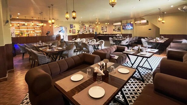 Ein Restaurant mit verschiedenen Essbereichen, darunter Sitzgelegenheiten in Boxen und an Tischen, mit hängenden Laternen.