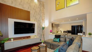 A modern living room with a large flat-screen TV, a grey sofa with teal cushions, wooden side tables, and a patterned rug. - CASA ESMERALDA, Refined duplex 120m2 (Panama)
