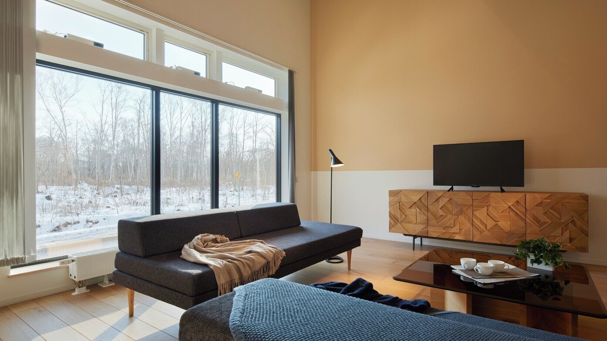 A modern living room with a large window, a sofa, a coffee table, and a TV on a wooden cabinet.