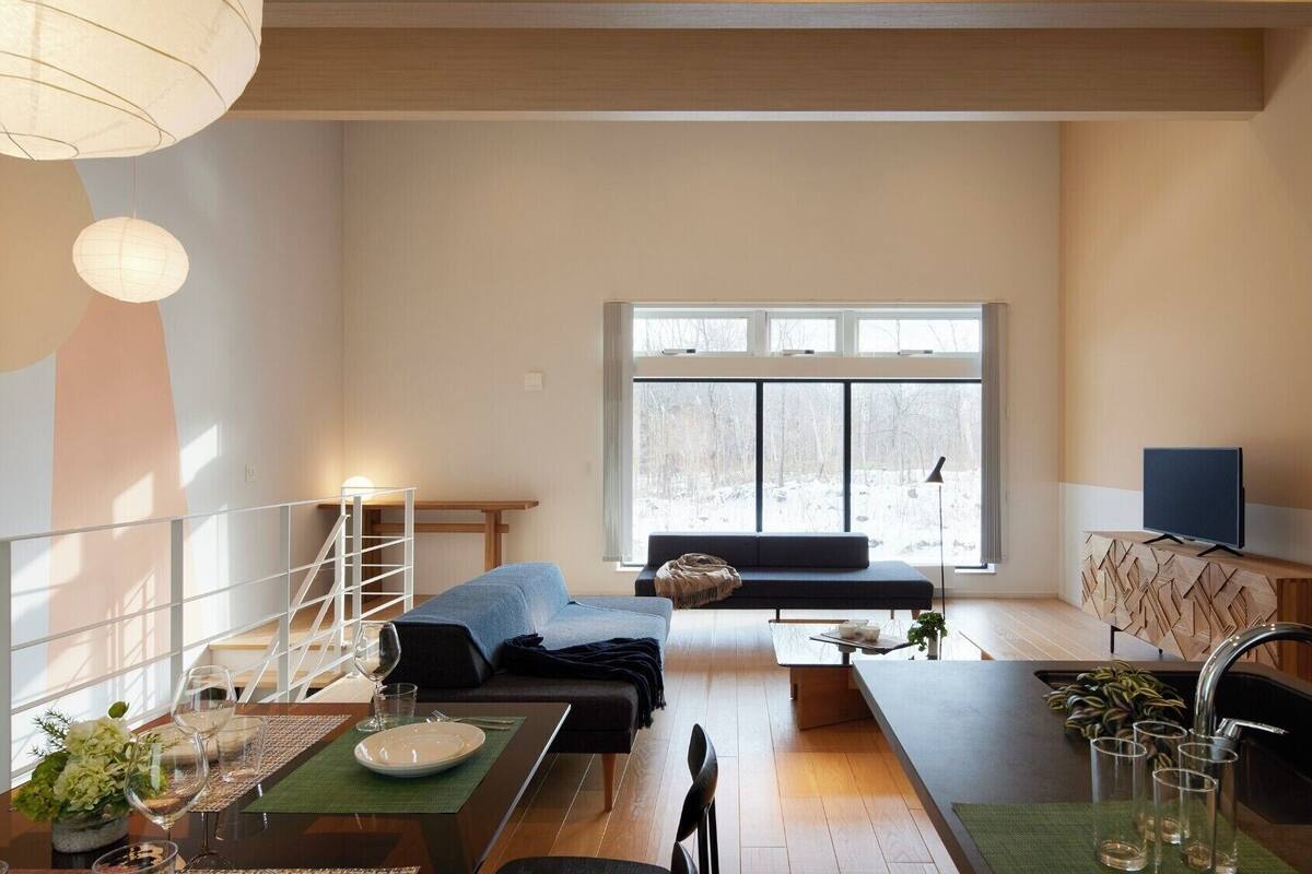 Una sala de estar moderna con comedor, ventanas amplias y un televisor sobre un mueble de madera.