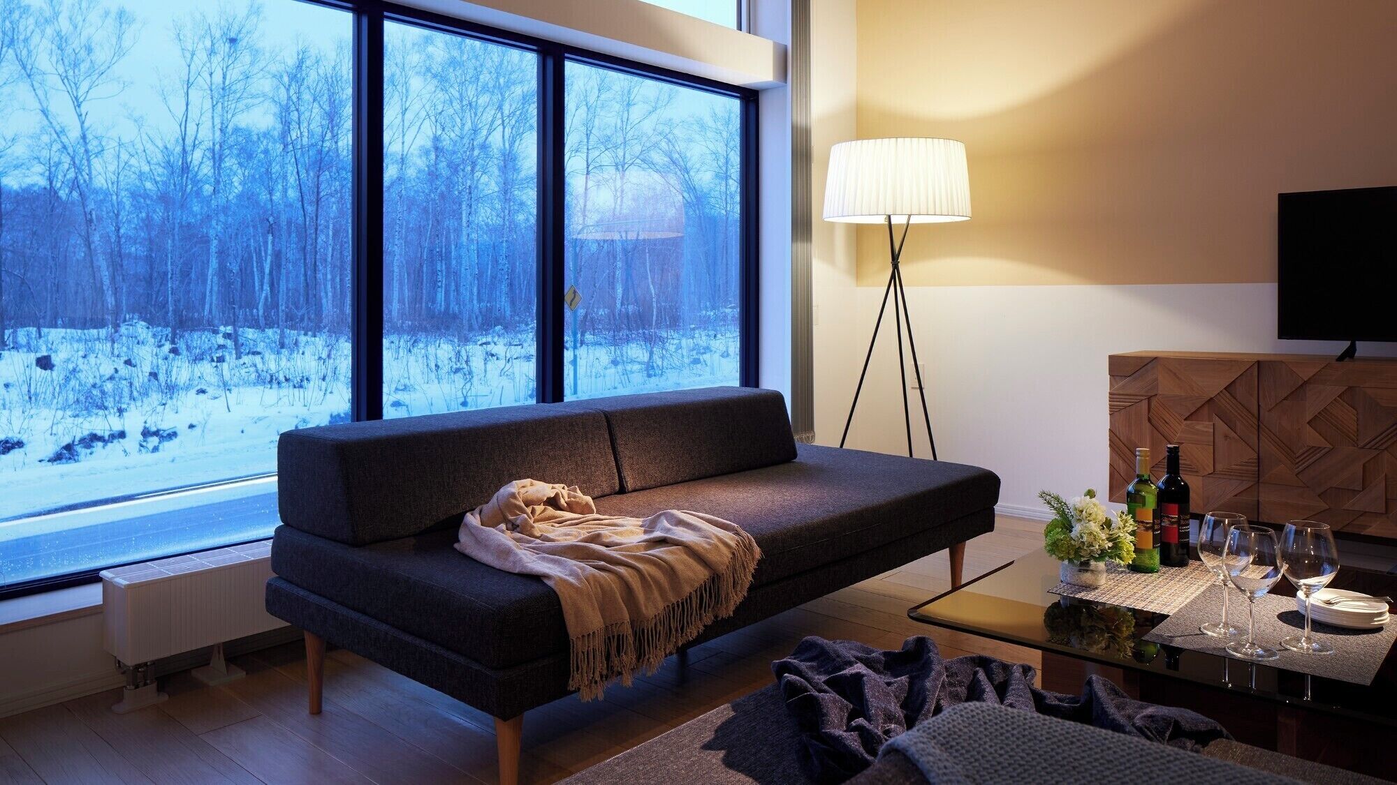 A modern living room with a large window, a sofa, a coffee table, and a TV.
