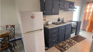 Eine kleine Küche mit dunklen Schränken, einem weißen Kühlschrank und einem Essbereich mit Tisch und Stühlen.