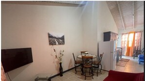 Ein Essbereich mit Tisch und Stühlen, einer Vase mit Blumen, einem an der Wand montierten Flachbildfernseher und einem roten Sofa.