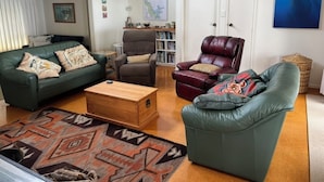 A living room with a green sofa, a brown armchair, a red leather chair, and a wooden coffee table. There is a map on the wall and a basket on the floor.