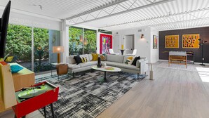 Ein modernes Wohnzimmer mit einer Couch, einem Couchtisch und einem roten Schrank. Große Fenster bieten Blick auf grüne Natur.