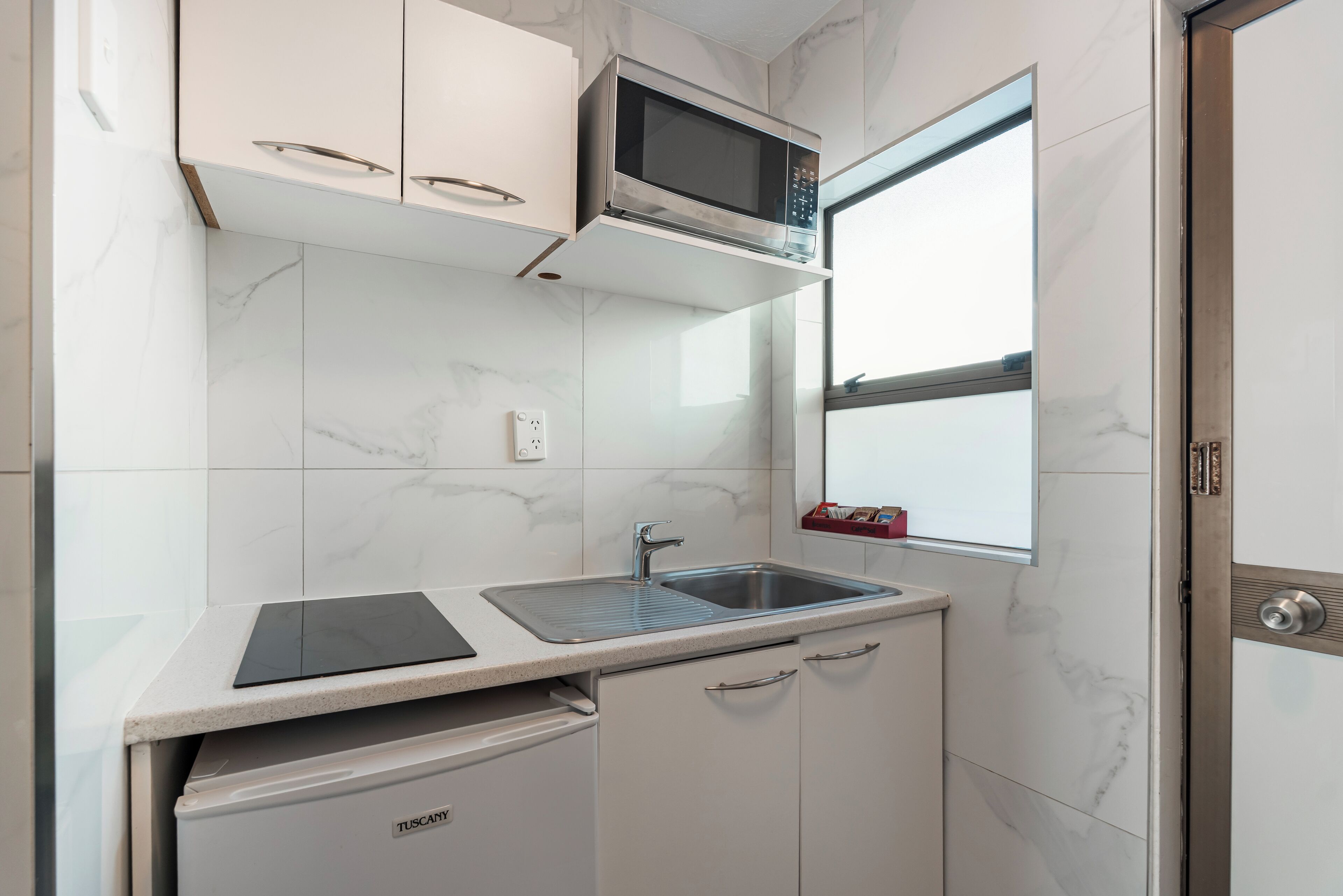 Una cocina compacta con microondas integrado, un lavabo y lavavajillas.