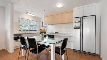 Una cocina moderna con una mesa de comedor de vidrio, cuatro sillas negras, un refrigerador de acero inoxidable y armarios de madera.