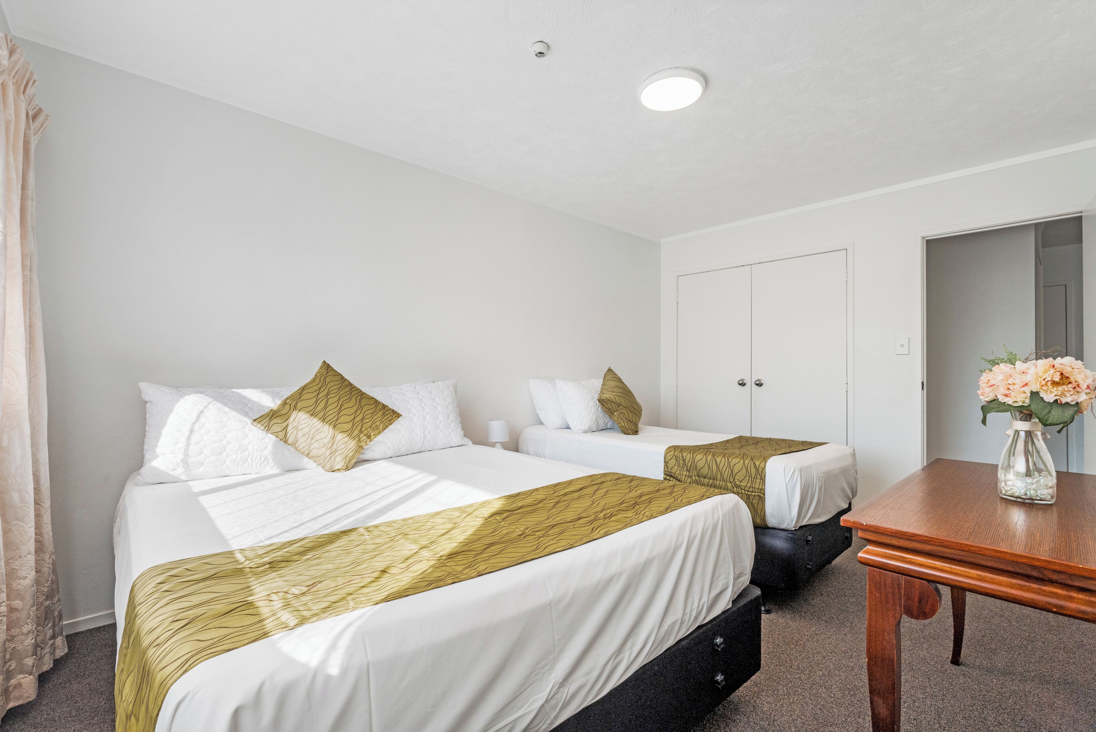 A hotel room with two beds, a wooden table, and a door.