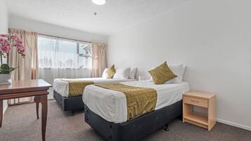 Ett hotellrum med två sängar, ett litet bord, ett sängbord och ett fönster med gardiner.