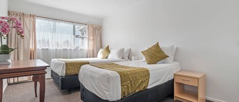 Una habitación de hotel con dos camas, una mesita, una mesita de noche y un ventanal con cortinas.