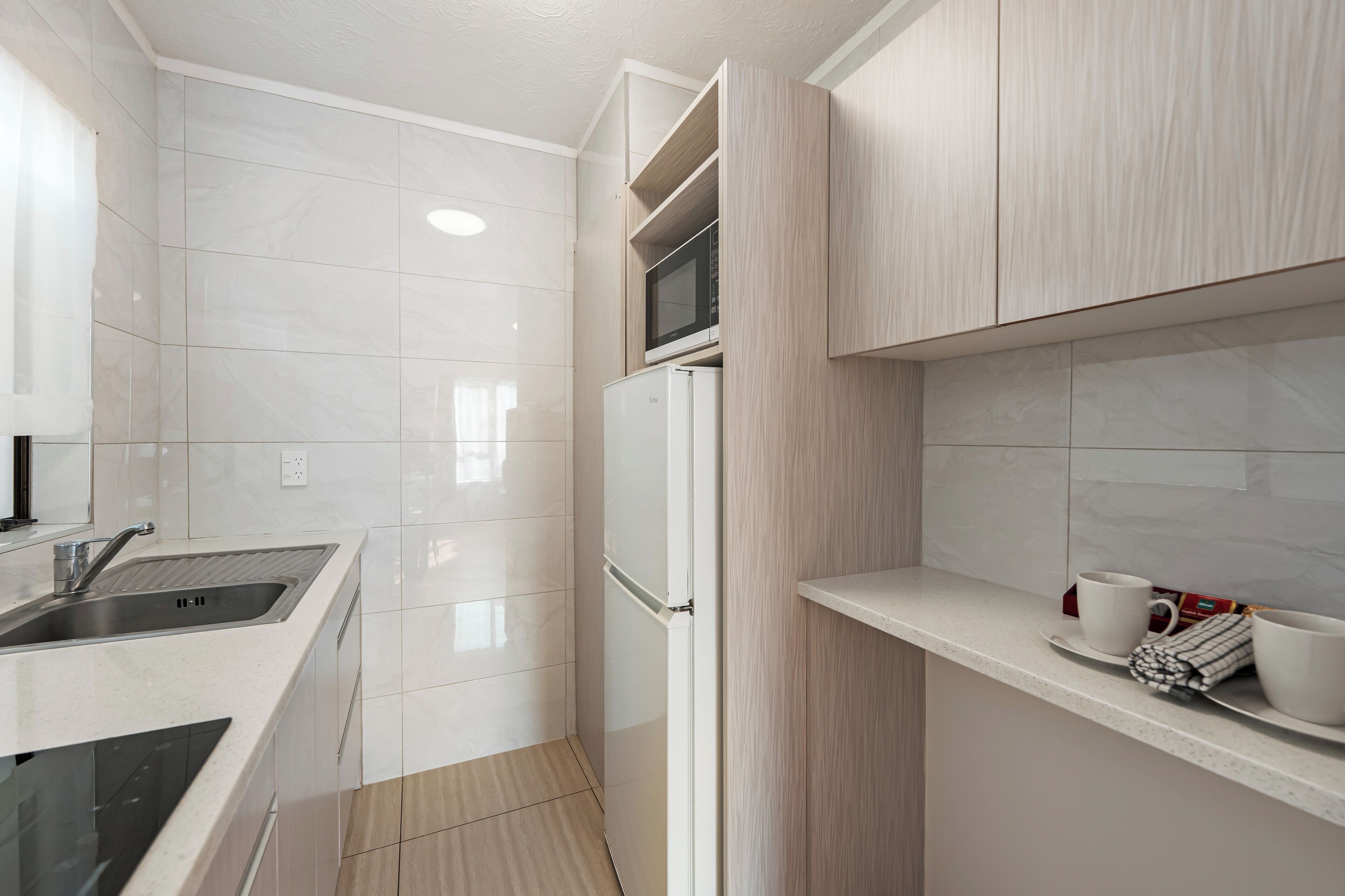 Una cocina moderna con armarios blancos, un lavamanos de acero inoxidable y un microondas en la encimera.