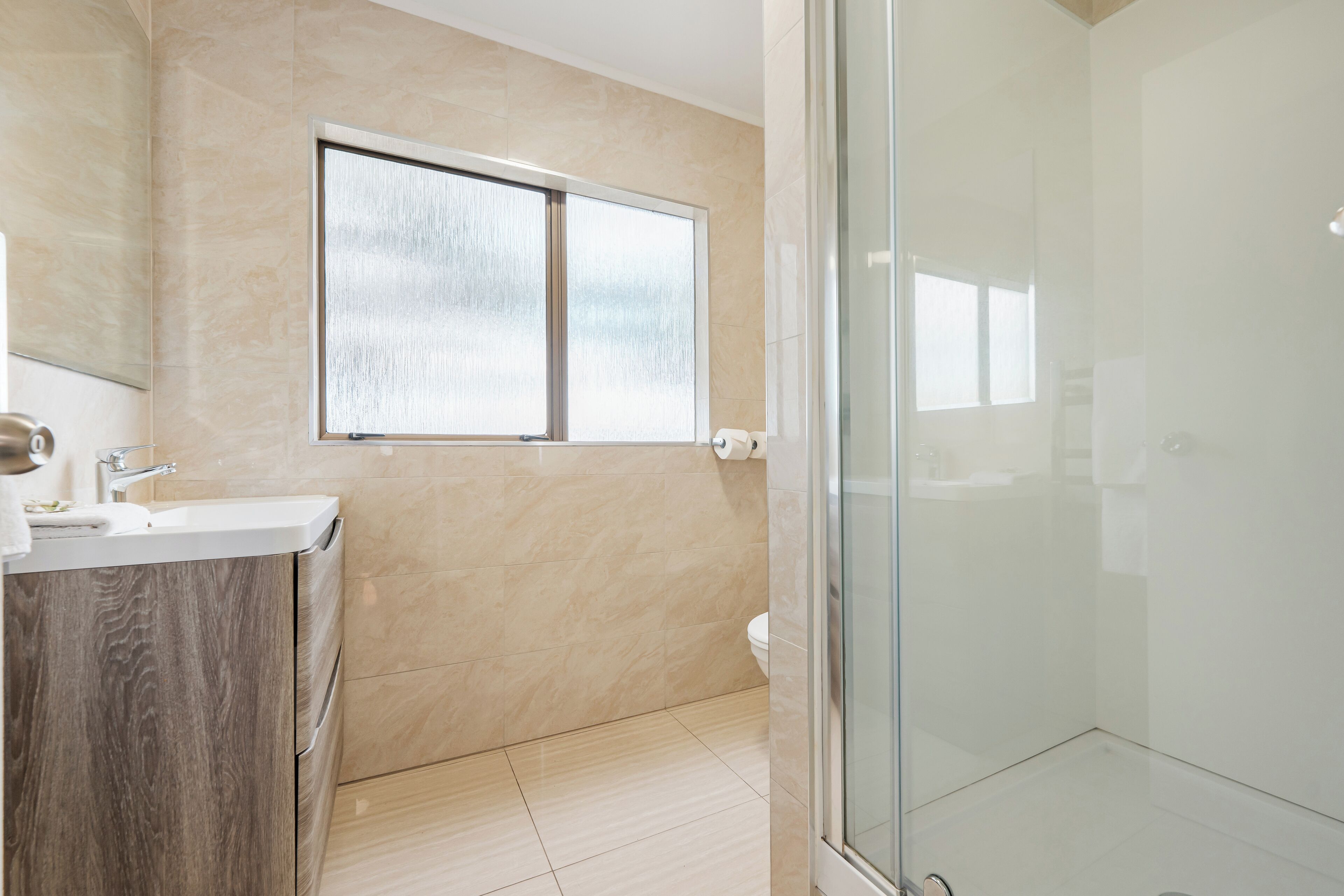 Un baño moderno con ducha de vidrio, un lavamanos con gabinete de madera y un inodoro.