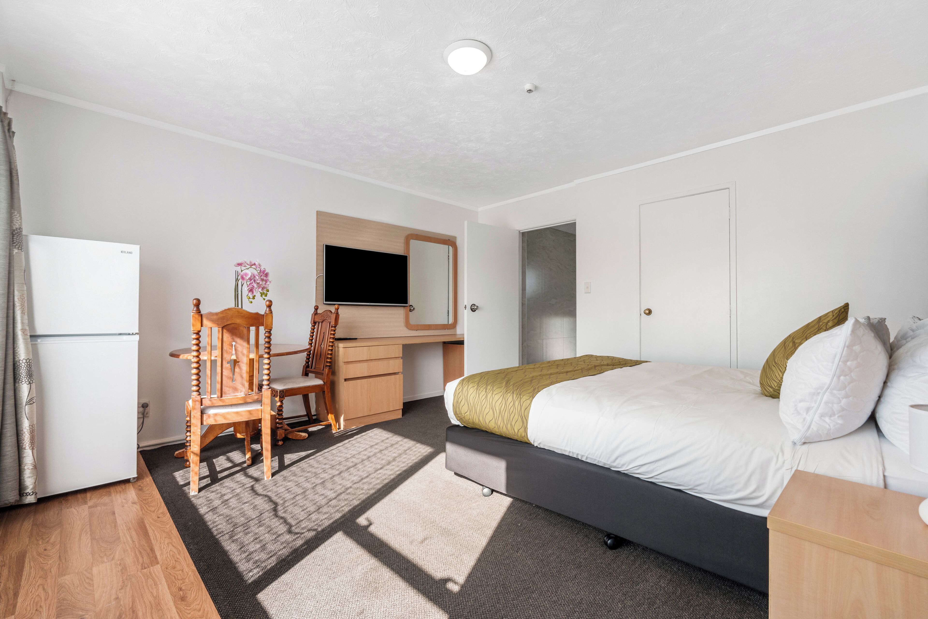 A hotel room with a bed, a desk, a chair, a TV, and a wardrobe.