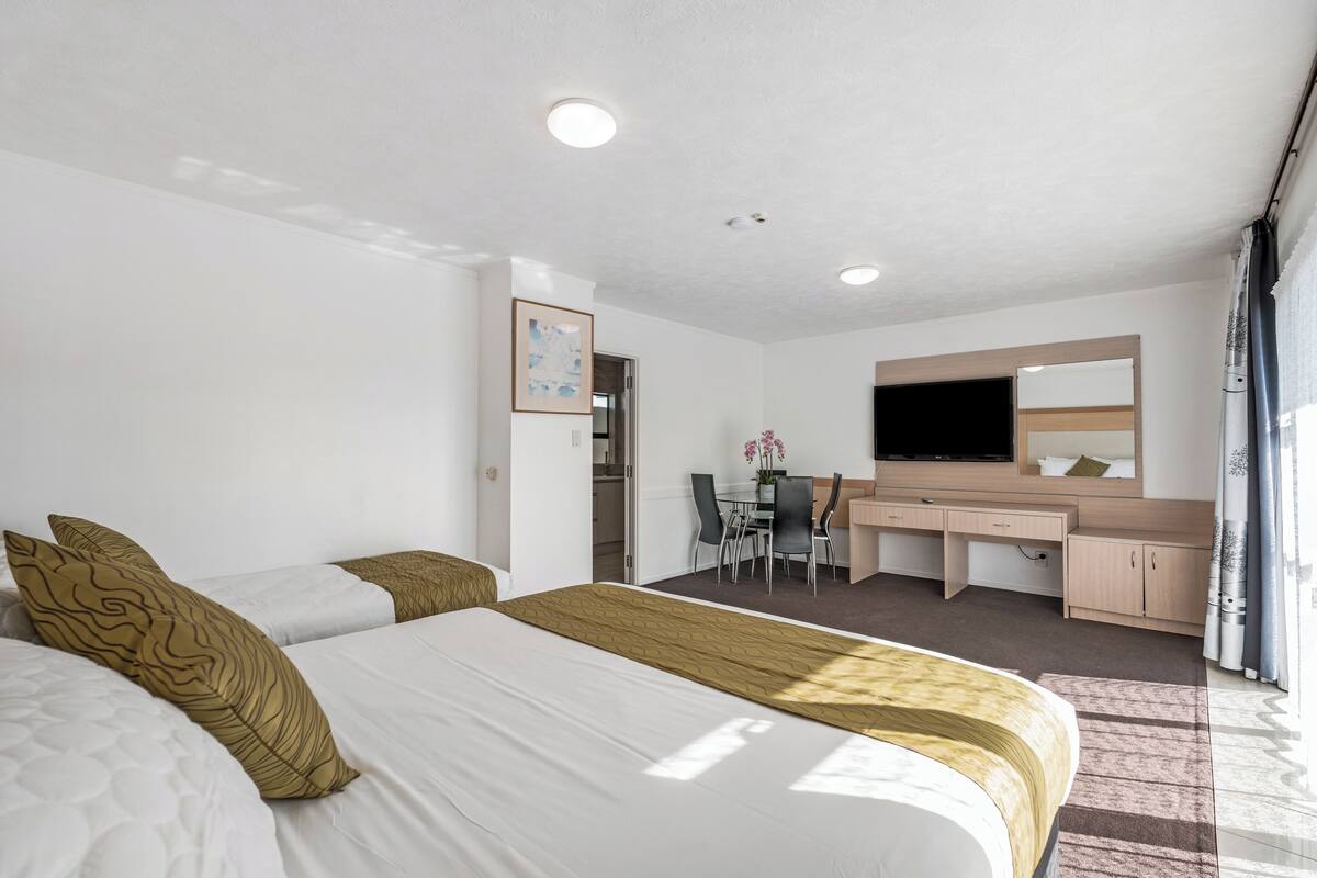 Une chambre d’hôtel avec un grand lit, un bureau avec une chaise, une télévision et une salle de bain visible à travers une porte ouverte.
