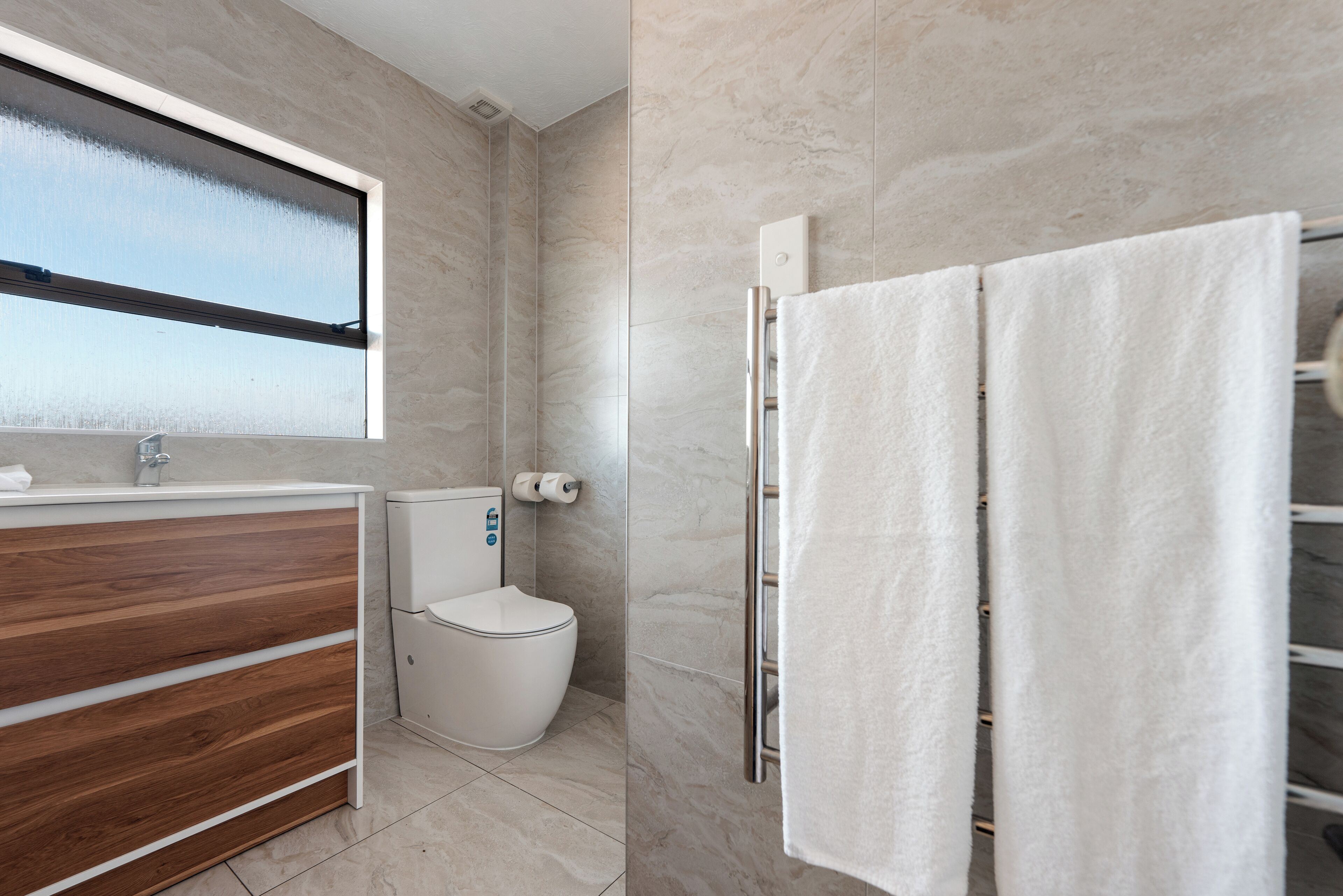Un baño moderno con tocador de madera, inodoro, perchero y ventana con vidrio esmerilado.