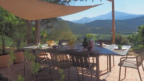 An outdoor dining area with a table set for four, surrounded by chairs, overlooking a mountainous landscape. - Charming house in the Dentelles de Montmirail. Ideal for recharging your batteries! (Suzette)
