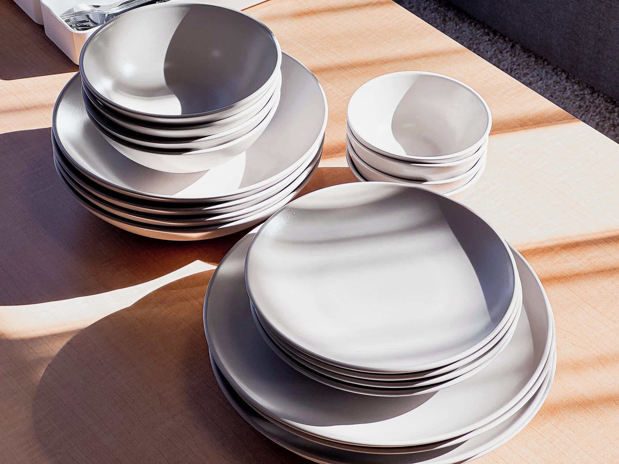A stack of white plates and bowls on a wooden table.