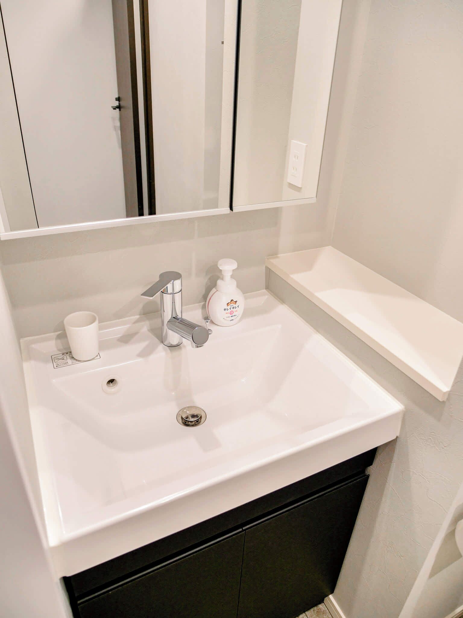 Une salle de bain avec un lavabo blanc, un miroir, un distributeur de savon et un gobelet.