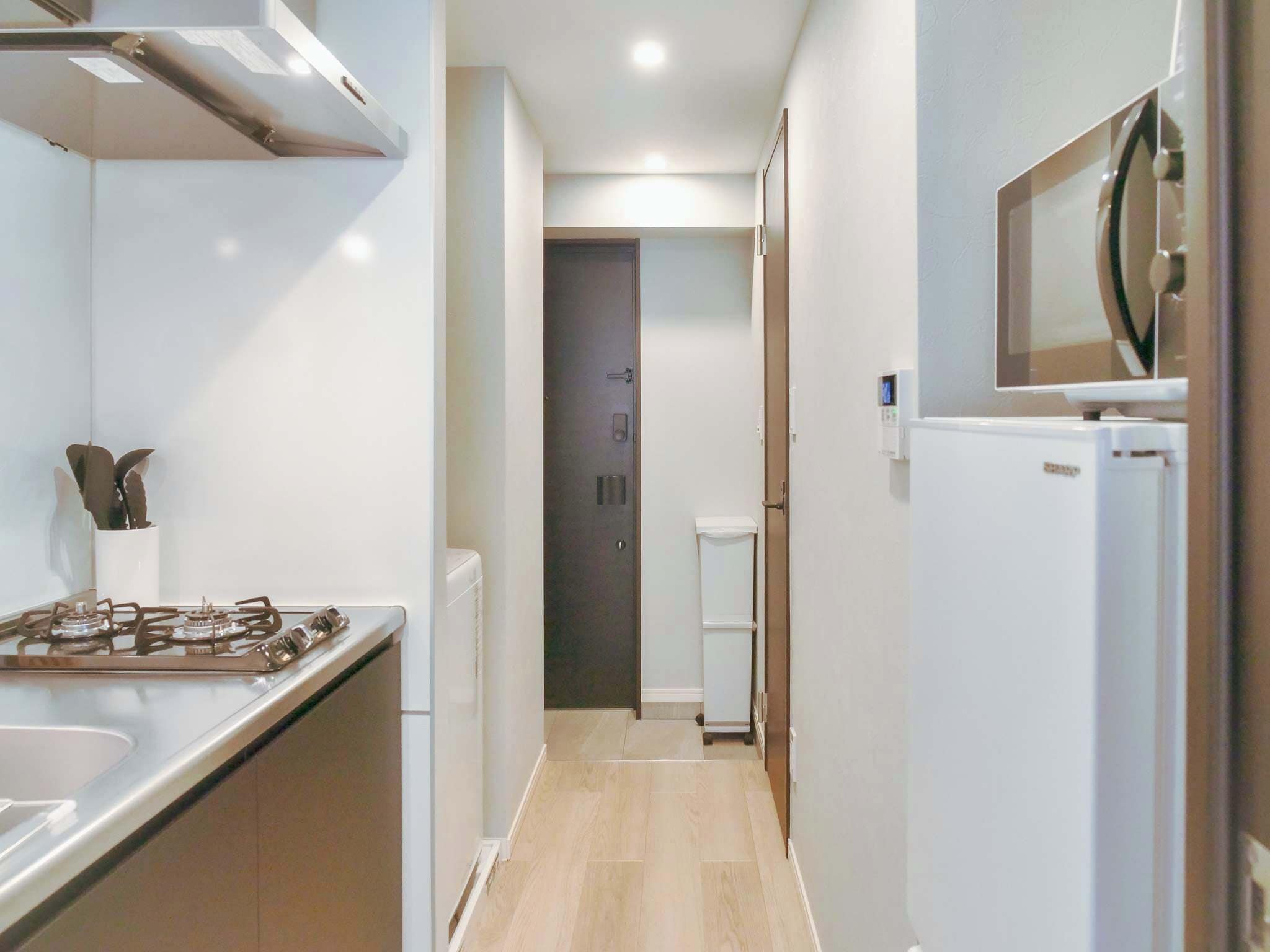 A narrow hallway with a gas stove, a white refrigerator, and a small toilet.