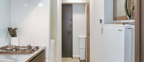 A narrow hallway with a gas stove, a white refrigerator, and a small toilet.