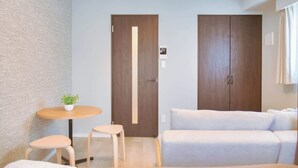 Une chambre d’hôtel moderne, équipée d’un lit, d’une petite table ronde avec deux tabourets, d’une plante en pot et d’une grande armoire.