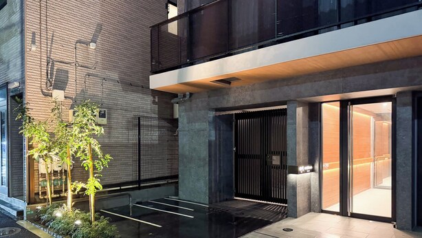 Un bâtiment moderne avec une façade en briques, une entrée sécurisée par un portail et un petit espace extérieur agrémenté de plantes.